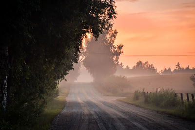 Road amidst trees against sky during sunset