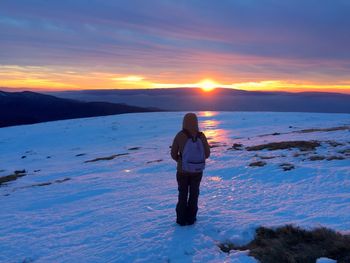 Rear view of woman standing on snow covered landscape during sunset