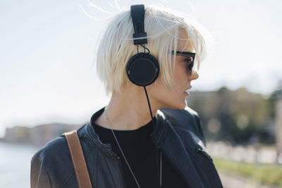Profile of blond woman wearing sunglasses listening music with headphones