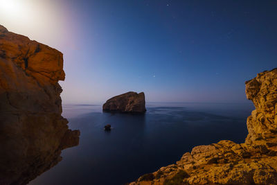 Rock formation in sea against sky at night