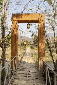 Empty footbridge in forest against sky