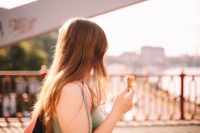 Young woman holding ice cream cone while walking on bridge in summer