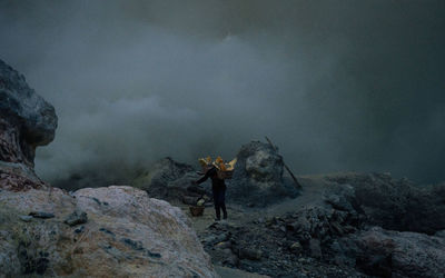 Rear view of man standing on rock by mountain