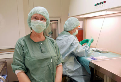 Portrait of female doctor standing by colleague working on table at hospital