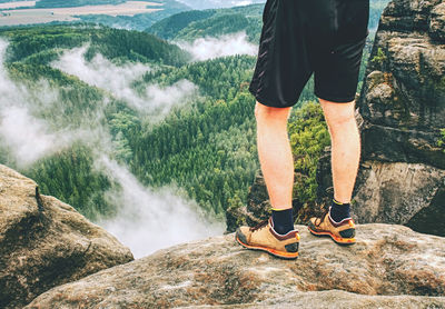 Fall nature with detail of hiker legs in low trekking black orange leather boots on summit