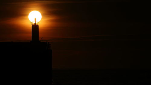 Silhouette lighthouse by sea against sky at sunset