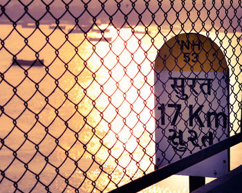 Close-up of chainlink fence against sky during sunset