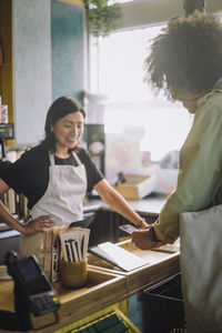 Smiling female sales clerk standing near male customer using mobile payment while scanning at store checkout counter