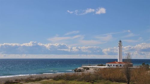 Lighthouse on beach against cloudy sky