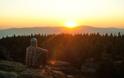 Rear view of man sitting on mountain against sky during sunset