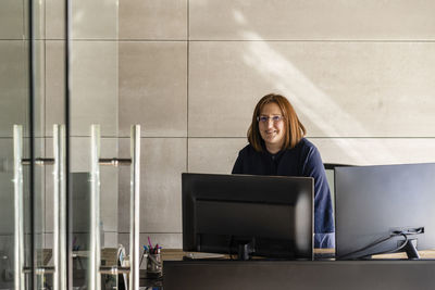 Smiling female entrepreneur with computer standing at desk in cabin