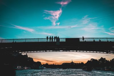 Silhouette people over river on bridge during sunset