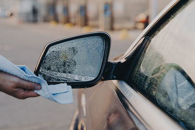 Close-up of hand holding sunglasses on side-view mirror