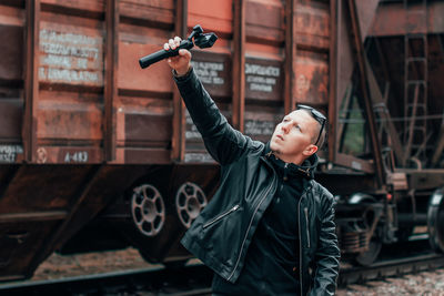 Young man blogging while standing against railroad car