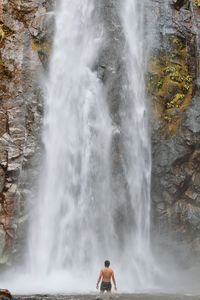 Rear view of shirtless man standing against waterfall