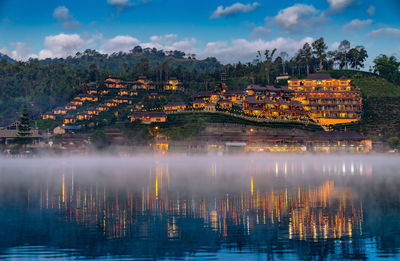 View of buildings by river against cloudy sky