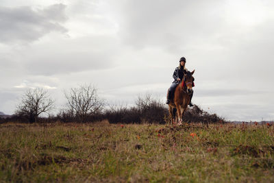 Woman riding horse on field against sky