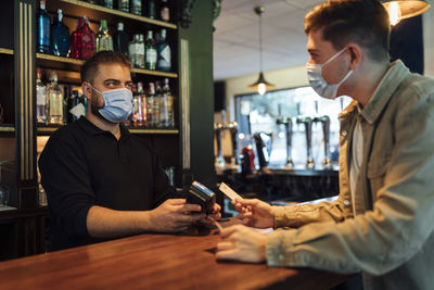 Young man holding camera while standing in cafe