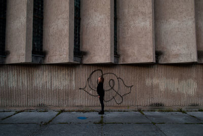 Side view of woman standing on footpath against building