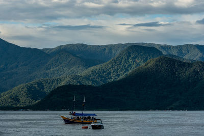 Sailboat sailing on sea by mountains against sky