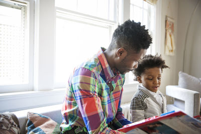 Father and young son reading book together at home