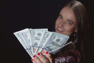 Portrait of smiling woman showing currency while standing against black background