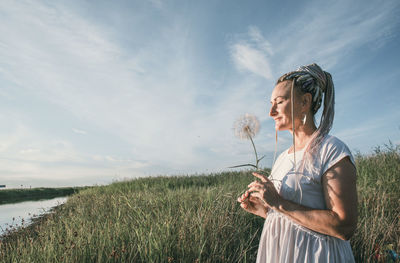 Girl with multicolored braids enjoys summer, face sideways, large dandelion