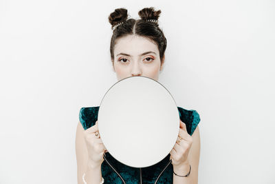 Portrait of woman holding mirror against white background