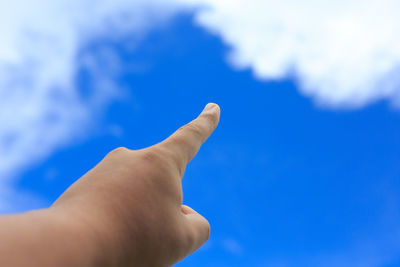 Cropped hand pointing against blue sky