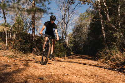 Male cyclist in protective helmet and goggles riding bicycle on pathway between trees during training in sunlight