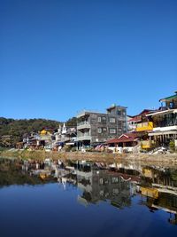 Reflection of buildings in lake against clear blue sky