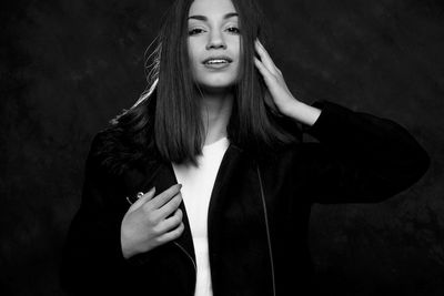 Portrait of smiling woman standing against black background