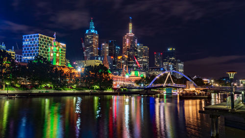 Illuminated city by river against sky