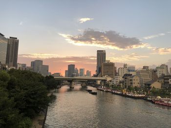 River amidst buildings in city against sky during sunset