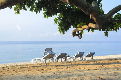 Empty chairs on beach by sea against sky