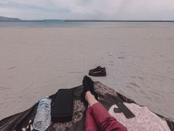 Low section of man relaxing on sand at beach against sky