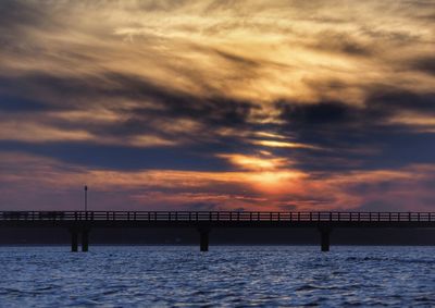 Bridge over sea against sunset sky