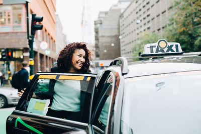 Smiling mid adult businesswoman entering taxi on street in city