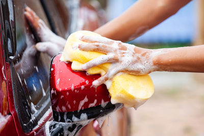 Cropped hands of woman cleaning car with cleaning sponge outdoors