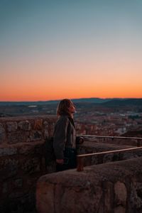 Rear view of man standing on retaining wall against sea during sunset