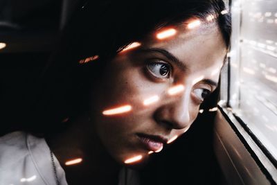 Close-up of thoughtful young woman looking through window at home