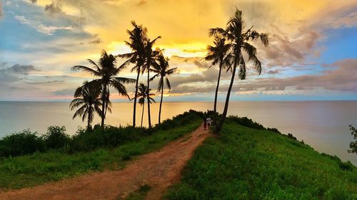 Dirt road by sea against cloudy sky during sunset