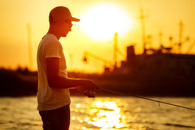 Side view of young man standing against sky during sunset