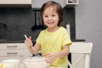 Little boy kneading dough with a whisk in the kitchen and smiling. time with children at home. 