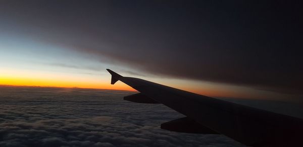 Airplane wing against sky during sunset