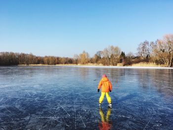 Rear view of child skating on ice rink against clear sky