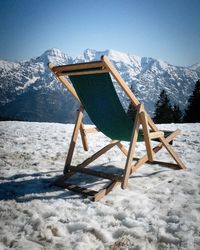 Chair on snow covered mountain against sky