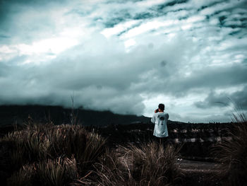 Rear view of man standing on land against storm clouds