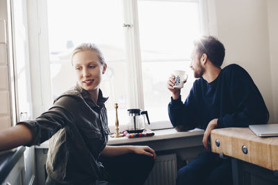 Couple sitting in kitchen drinking coffee by window at home