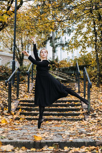 Ballerina dancing in autumn city street, modern ballet dancer in black dress, pointe shoes outdoors